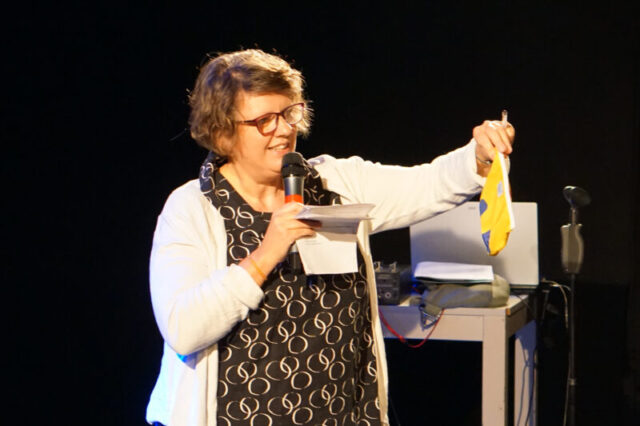 Barbara Sieberth, Geschäftsführerin im Friedensbüro, zeigt den Friedensbüro-Merch im Rahmen ihrer Festrede.